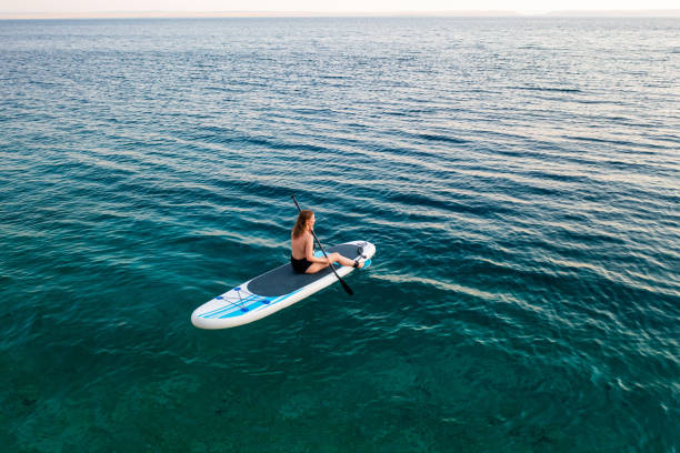 Woman paddle boarding on clear water during a calm twilight hour at the beach.